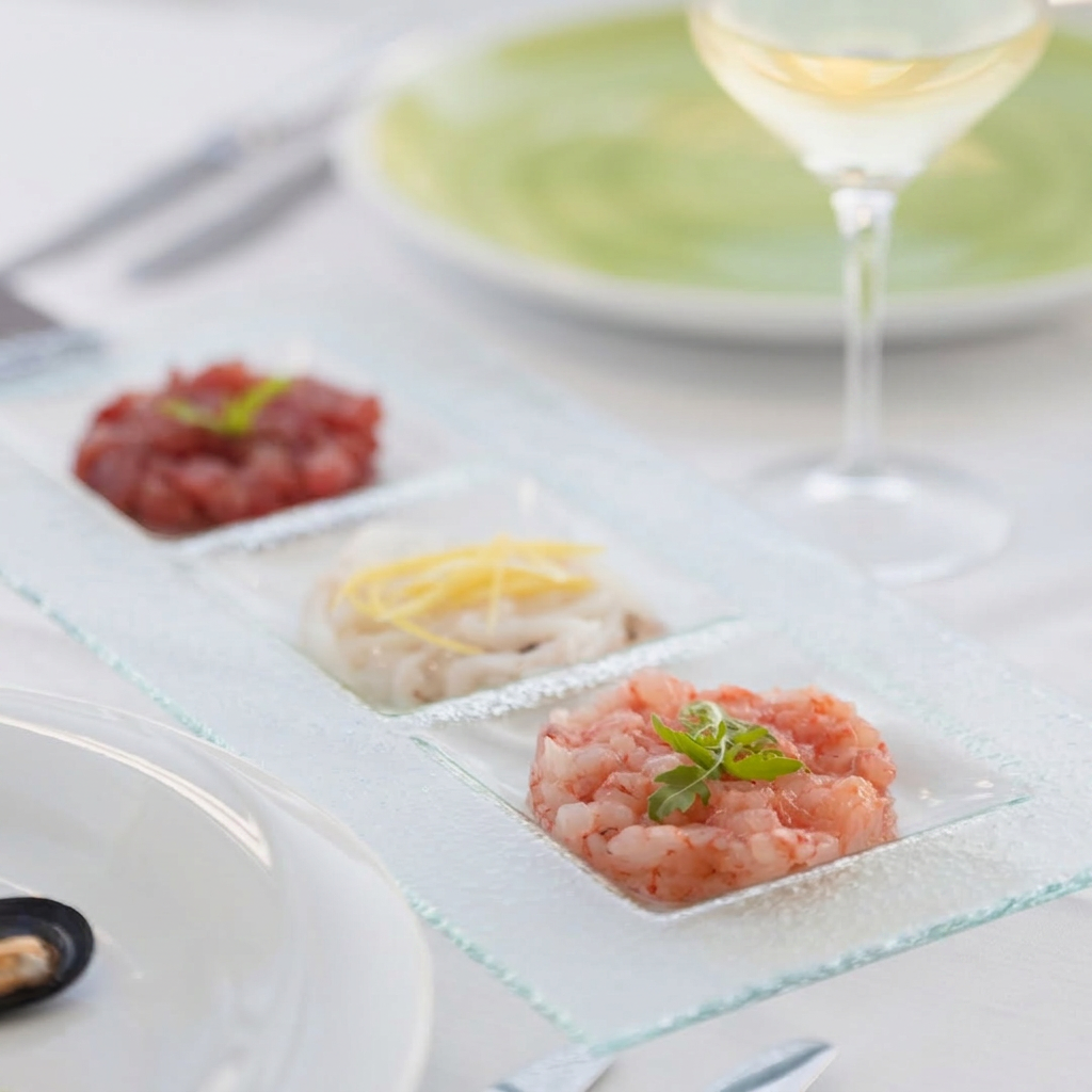 Tartare assortite di pesce crudo fresco presentate con eleganza e abbinate a un calice di vino